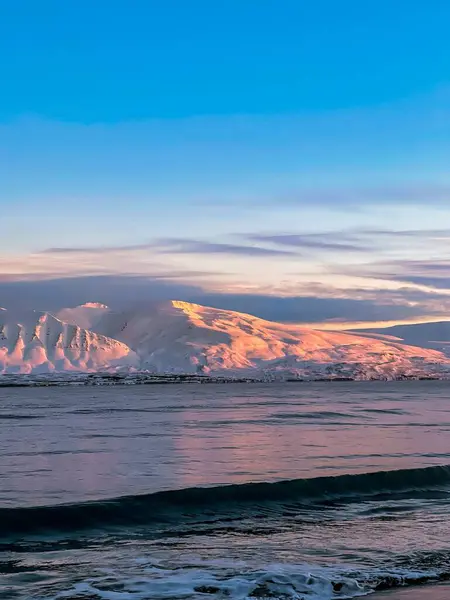 雪に覆われたアイスランドの日没時に海を渡って山を持つ牧歌的な風景 — ストック写真