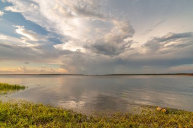 Gün batımında su yüzeyine yansıyan bulutlu bir nehrin manzarası.