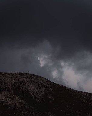 Kasvetli gökyüzünün altında İtalyan Dolomitlerine tırmanan bir yürüyüşçünün dikey görüntüsü.