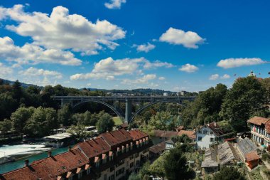 Bern 'ün kırmızı kiremitli binaları, yemyeşil ağaçları ve arka planda bir köprüsü olan insansız hava aracı görüntüsü.