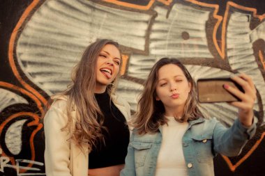 Sokakta gülümseyen ve selfie çeken iki bayan arkadaş.