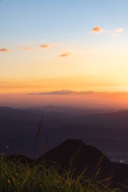 Turuncu gökyüzünün altında ufka uzanan dağlık bir manzaranın dikey görüntüsü