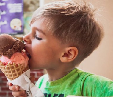 Arka planda bulanık bir külah dondurma yiyen genç bir çocuğun yakın çekimi.