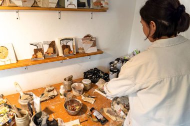 Dağınık stüdyosunda sanat üzerine çalışan genç bir kadın sanatçının yüksek açılı çekimi.