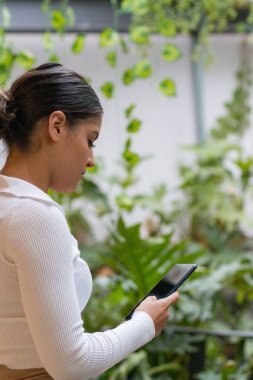 Bahçede dikilen ve telefonunu kullanan genç bir İspanyol kadın.