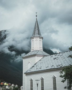 Norveç 'teki beyaz Hyen kilisesinin dikey görüntüsü. Arka planda bir bulutun arkasında saklanan bir dağ.
