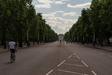 Güneşli bir günde insanların yürüdüğü ve bisiklete bindiği Buckingham Sarayı yolu.