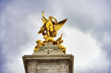Kraliçe Victoria Memorial 'ın düşük açılı çekimi. Londra, Buckingham Sarayı yakınlarında bulutlu gökyüzünün altında altın kanatlı bir melek heykeli.