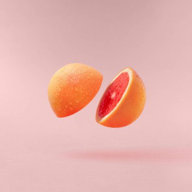 Yarı yarıya kesilmiş bir greyfurt pastel pembe bir arka plana doğru uçuyor..
