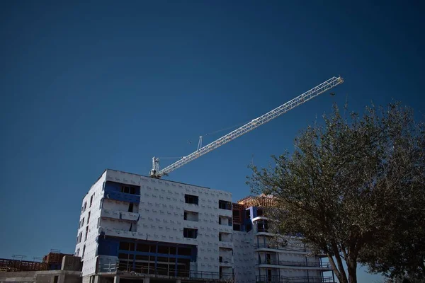 青い空を背景に建物の後ろの建設クレーンの眺め — ストック写真