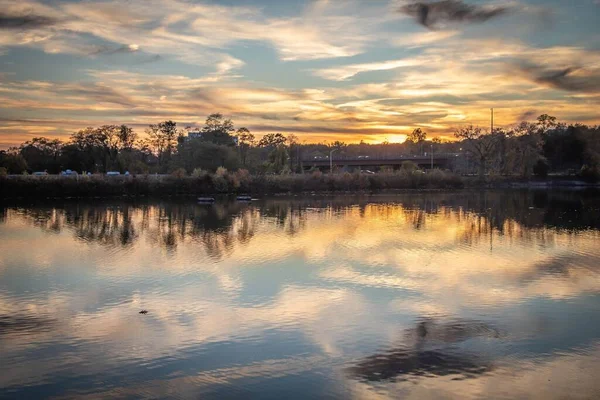 夕日の上のカラフルな曇り空を反映した街の静かな湖の豪華な景色 — ストック写真