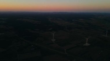 Türkiye 'de gün batımında bir tarlada rüzgar türbinlerinin yavaşça dönüşünü gösteren hava manzarası