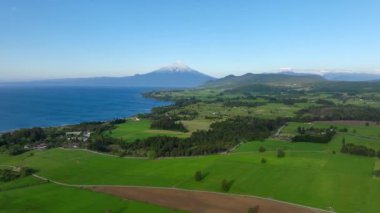 Tarlaları göl ve arkaplanda yanardağ olan güzel bir manzaranın drone görüntüsü.