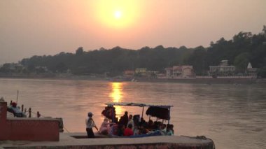 Rishikesh, Hindistan - 18 Ekim 2022 - Bir grup insan gün batımında Ganj nehrinde bir tekneye biniyorlar.