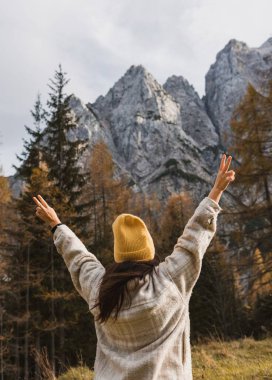 Slovenya 'daki Vrsiç dağ geçidinde sonbaharda güzel dağların altında duran kollarını kaldırmış genç bir kadının arka manzarası
