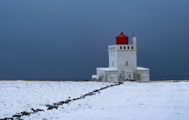 İzlanda 'daki Dyrholaey deniz feneri gri kasvetli gökyüzüne karşı karlı bir tarlayla çevrili.