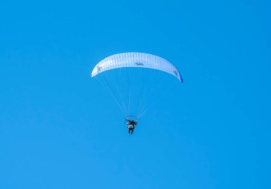 Yeni Zelanda 'da mavi gökyüzü ve beyaz kanatlı bir sahil boyunca tek başına uçan güçlü bir paraglider. Motor pi tarafından giyilir.