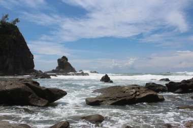 Bulutların altında kayalar olan güzel bir deniz manzarası.
