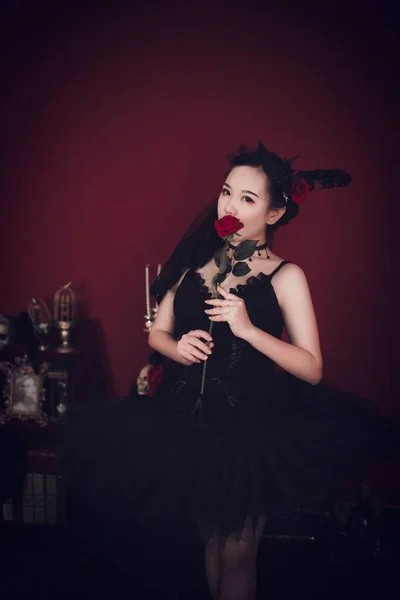 stock image A vertical shot of a beautiful east Asian girl wearing a tutu black dress and holding a rose while looking at the camera