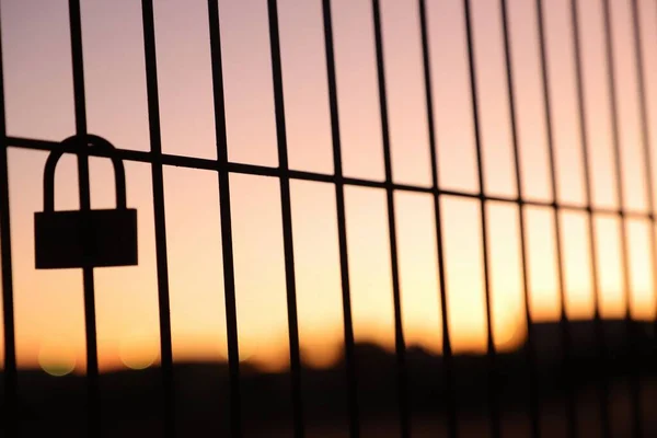 赤い空の日没の背景にフェンスの上に置かれた南京錠 — ストック写真
