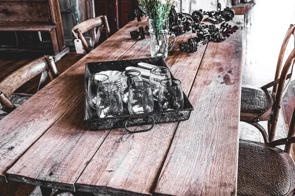 大きな木製の板農家のテーブルには トレイや遭難椅子を提供するガラスカップがあります — ストック写真