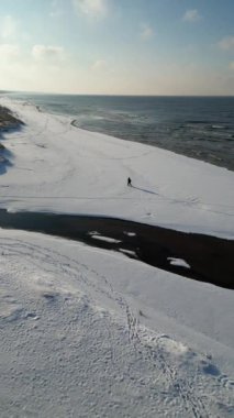 Mavi gökyüzüne karşı dalgalarla karlı sahilin dikey görüntüsü.