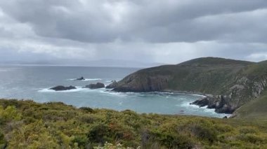 Okyanus dalgası bir dağın tepesinden deniz suyuyla birlikte bulutlu mavi bir gökyüzünün altında görünüyor.
