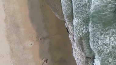 Sahile vuran köpüklü deniz dalgaları ve arka planda parlak mavi bir gökyüzü.