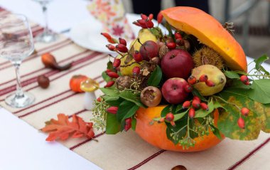 Sonbahar temalı bir dekorasyonun seçici odak noktası. Parti masasındaki balkabağında meyve ve yapraklar.