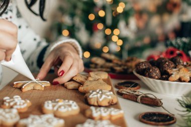 Boru torbası tutan kadın, ev yapımı Noel kurabiyelerini beyaz kraliyet kremasıyla süslüyor.