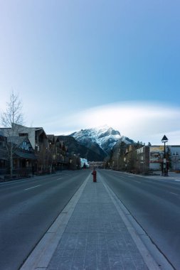 Banff, Alberta 'da evlerle ve güzel karlı dağlarla çevrili boş bir yolun dikey görüntüsü.