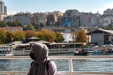 Türban ve yüz maskesi takan genç bir Müslüman kadın İstanbul, Türkiye 'de feribotla seyahat ediyor.