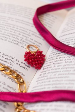 Açık bir kitap sayfasında kalp kolyesinin dikey görüntüsü.