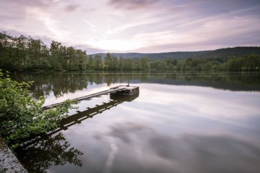 Etrafı yeşil ağaçlarla çevrili, arka planda dramatik bir gökyüzü olan küçük bir iskele.