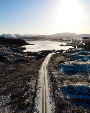 Karlı vadiden geçip İskoçya 'da gün doğumunda dondurucu göle giden yol manzaralı bir kış manzarası