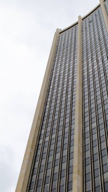 Bulutlu gökyüzüne karşı modern ve yüksek bir gökdelenin ön cephesi