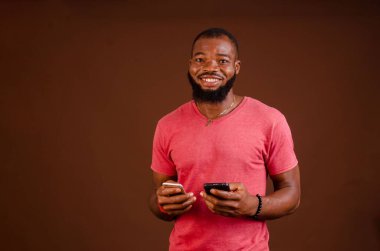 Kırmızı duvara akıllı telefonlar dayayan mutlu bir Nijeryalı erkek.