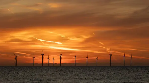 stock image Rich orange sky over an offshore windfarm in the North Sea. Wind turbines are silhouetted against the colourful sky.