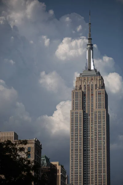 A vertical shot of the Empire State Building under the half-cloudy, blue sky in New York City, Manhattan