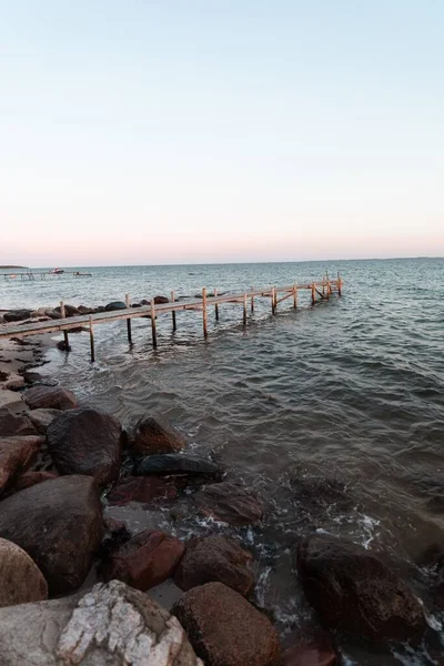 丹麦落日时在岩石海岸上的一个木制码头的垂直截图 — 图库照片