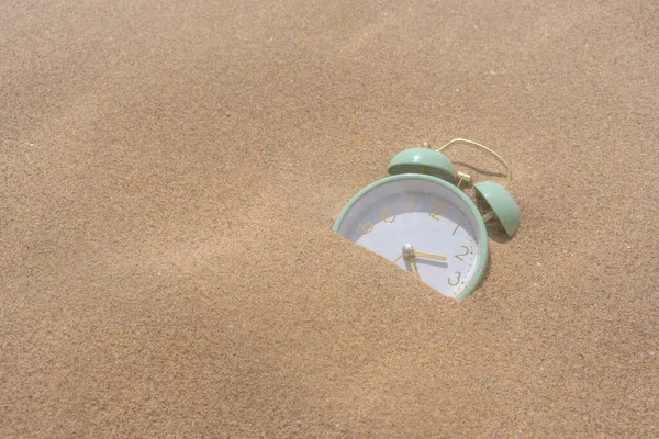 一个绿色闹钟的特写镜头 它被沙粒覆盖了一半 — 图库照片