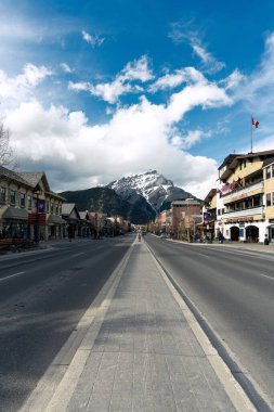 Banff, Alberta 'da evlerle ve güzel karlı dağlarla çevrili boş bir yolun dikey görüntüsü.
