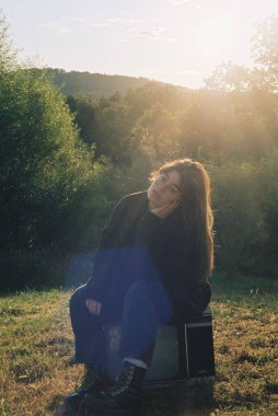 Parktaki eski bir televizyona oturup poz veren bir kadının dikey görüntüsü.