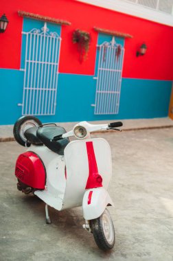 Kırmızı ve mavi bir duvarın önüne park edilmiş Vespa mobiletinin dikey görüntüsü.