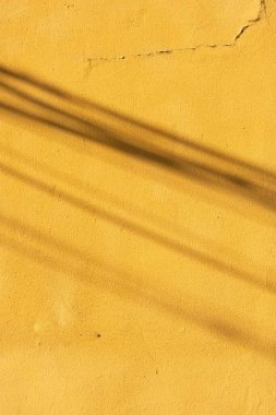Üzerinde gölgeler olan sarı çatlamış bir duvarın dikey görüntüsü.
