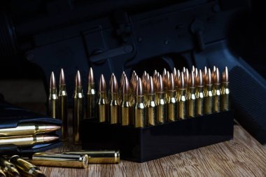 Kutudaki 5.56x45 mm 'lik mermiler gevşek bir şekilde dizilmiş ve bambu bir tahtanın üzerinde AR-15 şarjöründe.