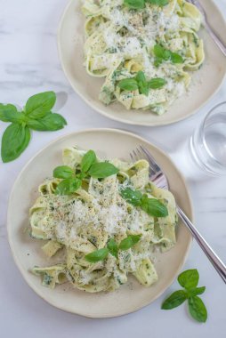 Masada fesleğen ve parmesan peynirli iki tabak pesto makarna.
