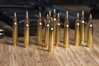 Dolu bir AR-15 tüfeğinin önünde, bambu tahtanın üzerinde duran 5.56 mm 'lik parlak mermiler.