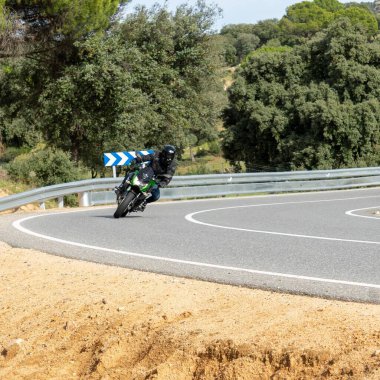 Siyah kıyafetli ve mavi kasklı bir erkek sessiz bir sokakta motosiklet sürüyor.