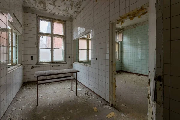 放棄された場所にテーブルと引き裂かれたセラミック壁を持つ空の減衰部屋 — ストック写真